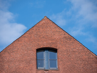 Giebel eines rot verklinkerten Hauses mit kleinem Fester vor blauem Himmel