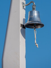 alte Schiffsglocke an einem weißen Mast vor blauem Himmel