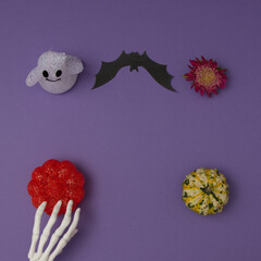 Halloween decoration with pumpkin and flower, bat and hand skeleton on purple background with copy space and spirit. Flat lay composition.