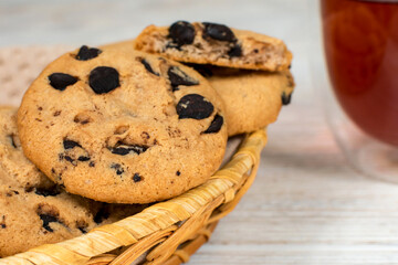 Chocolate cookies in a basket close-up on the background of a glass cup of tea on a white wooden table.