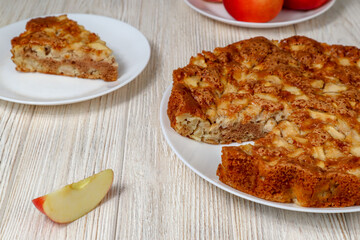 Apple pie on a plate on a wooden table against a background of red apples.