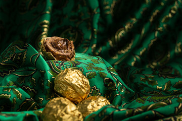 Tasty Chocolate Praline Wrapped with Golden Foil on Gorgeous Green Backdrop