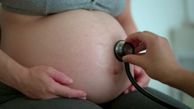checking asian pregnant women’s belly with stethoscope
