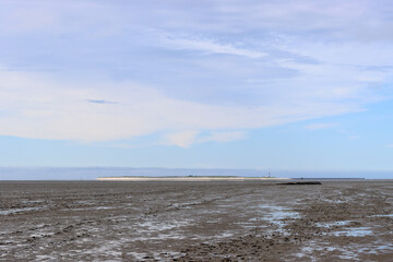 Low tide in the Wadden Sea of ​​the North Sea near Schillig with a view of the East Frisian island of Minsener Oog in Germany with a blue cloudy sky in a tranquil scene