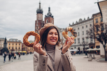 Woman eating bagel obwarzanek traditional polish cuisine snack on Market square in Krakow. Travel Europe in autumn