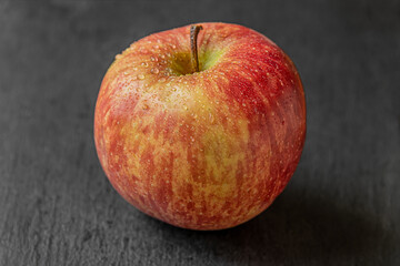 juicy organic red apple in drops of water on a black slate surface close up