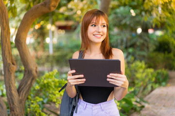 Fototapeta premium Young pretty redhead woman at outdoors holding a tablet