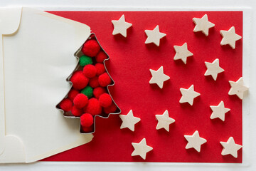 envelope with christmas tree cookie cutter, pom poms and plain wooden hearts on red 