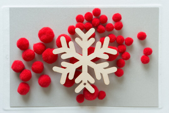 Wooden Snowflake Ornament On A Group Of Red Pom Poms