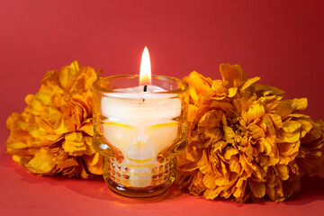 Veladora de calavera con flores de cempasúchil sobre fondo naranja.