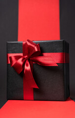 Male gift in black paper with red bright bow on a dark background. Black friday concept.