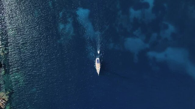 clear blue sea, sailboat pulling small inflatable boat behind. the focus is on the boat sailing over the water. drone aerial shot birds eye view.