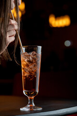 Beautiful young woman is drinking rum cola cocktail with a straw, dark elegant photo, a part of face visible