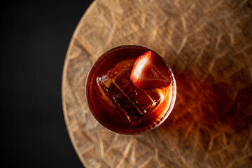 Top view of strawberry negroni on textured wooden board, muffled light