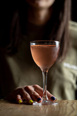 Beautiful young woman is holding a glass with cocktail in a dark bar, face is partly visible, atmospheric lonely photo