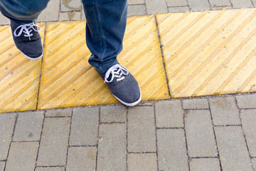 men's feet on the sidewalk with a bright yellow tactile coating on for people with poor eyesight....