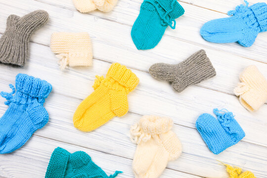 baby clothes knitted booties on a white wooden background. View from above - Image