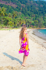 A woman with long blond hair walks along the sandy seashore on the tropical island of Koh Chang in Thailand. Travel and tourism.