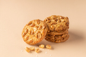 Stack of crunchy cookies with roasted peanuts on top on beige background. Front view. Place for text.