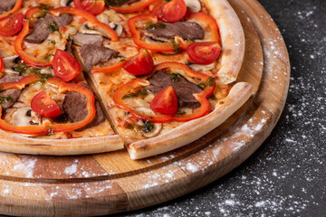 Pizza with paprika, meat and tomatoes on a wooden desk