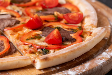 Slice of pizza with paprika, meat and tomatoes on the wooden board