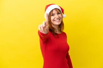 Redhead girl with christmas hat isolated on yellow background showing and lifting a finger
