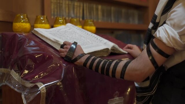 A Jew prays in the synagogue. A man stands near the presidium and reads a book. The camera is getting closer.
