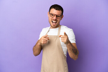 Brazilian restaurant waiter over isolated purple background pointing to the front and smiling