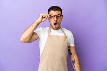 Brazilian restaurant waiter over isolated purple background with glasses and surprised