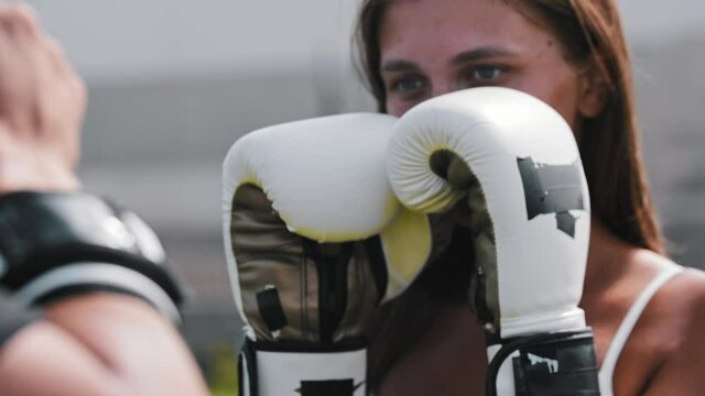 Young woman in boxer gloves punching in mitts