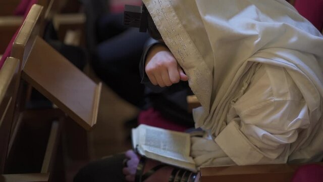 An adult man, a Jew, reads a book while closing his eyes. Prayer, tefillin, tallit