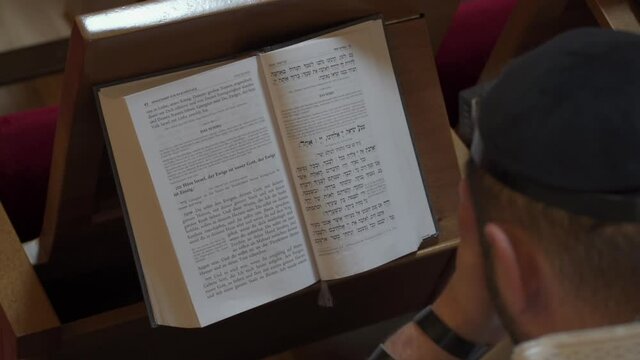 An adult man, a Jew, reads a book while closing his eyes. Prayer, tefillin, tallit. View from above