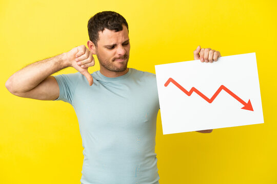 Brazilian man over isolated purple background holding a sign with a decreasing statistics arrow symbol and doing bad signal