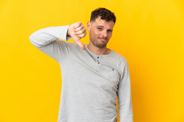 Young caucasian handsome man isolated on yellow background showing thumb down with negative...