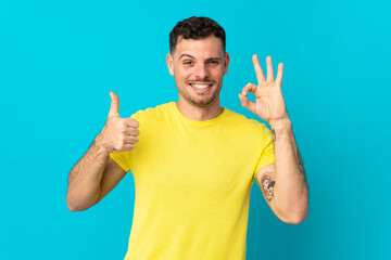Fototapeta premium Young caucasian handsome man isolated on blue background showing ok sign and thumb up gesture