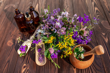 Summer medicinal herbs - St. John's wort, chamomile, clover near wooden mortar. Bottles for...