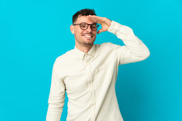 Young caucasian handsome man isolated on blue background looking far away with hand to look something