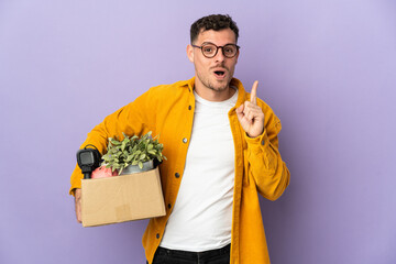 Young caucasian man making a move while picking up a box full of things isolated on purple...
