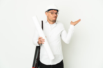 Young architect man with helmet and holding blueprints isolated on white background having doubts while raising hands