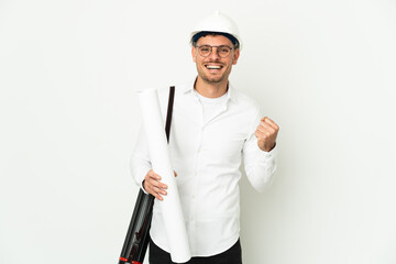 Young architect man with helmet and holding blueprints isolated on white background celebrating a victory in winner position