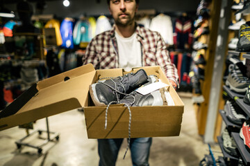 Store clerk helping customer try hiking boots at outdoors equipment shop. Salesman demonstrating...