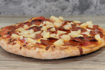 Freshly baked pineapple and pepperoni pizza with chopped vegetable toppings served on a wooden...