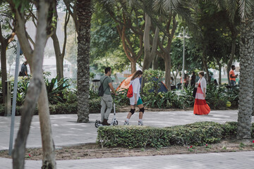 People walking at the park. Kids play and adults go around in the fair with green grass, palms, emerald trees, interesting flag decoration. Families enjoy and spend time together. 