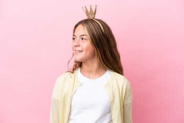 Little princess with crown isolated on pink background looking to the side and smiling