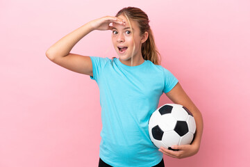 Little football player girl isolated on pink background doing surprise gesture while looking to the side