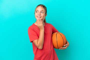 Little caucasian girl playing basketball isolated on blue background looking up while smiling