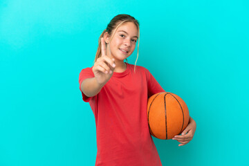 Little caucasian girl playing basketball isolated on blue background showing and lifting a finger