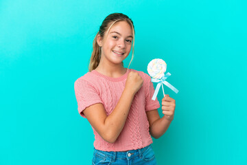 Little Caucasian girl holding a lollipop isolated on blue background celebrating a victory