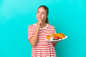 Little caucasian girl holding waffles isolated on blue background and looking up