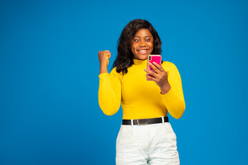 beautiful young black woman using her phone rejoicing